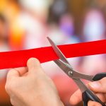 Hand with scissors cutting red ribbon - opening ceremony